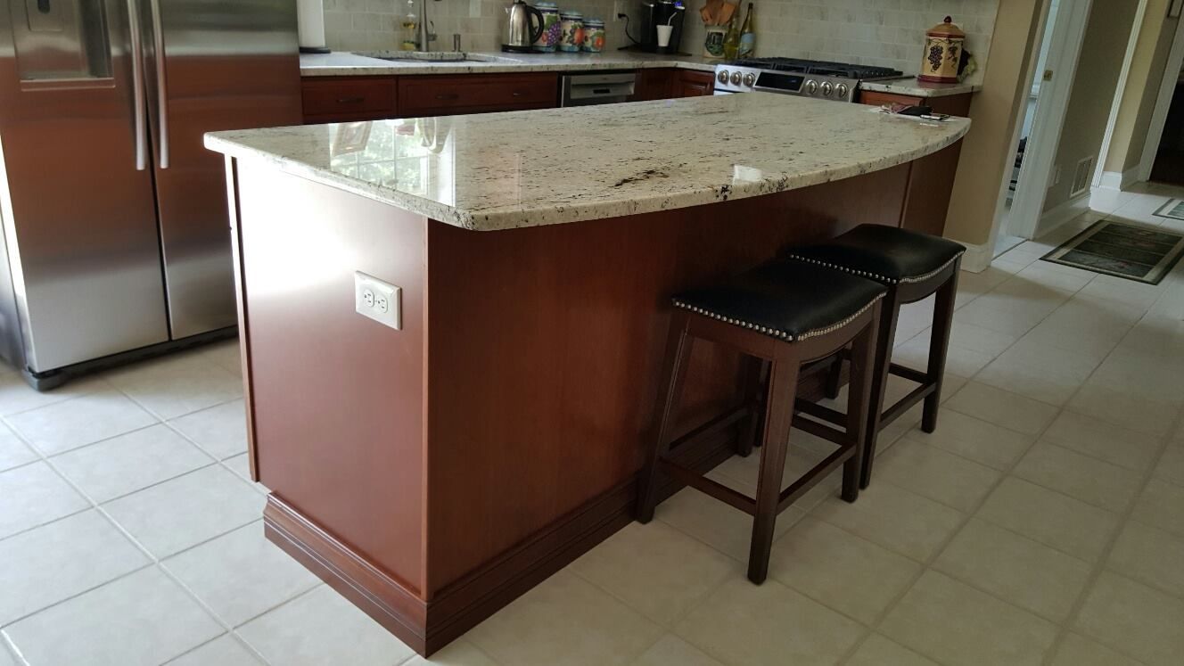 A kitchen with a large island and stools and a stainless steel refrigerator.