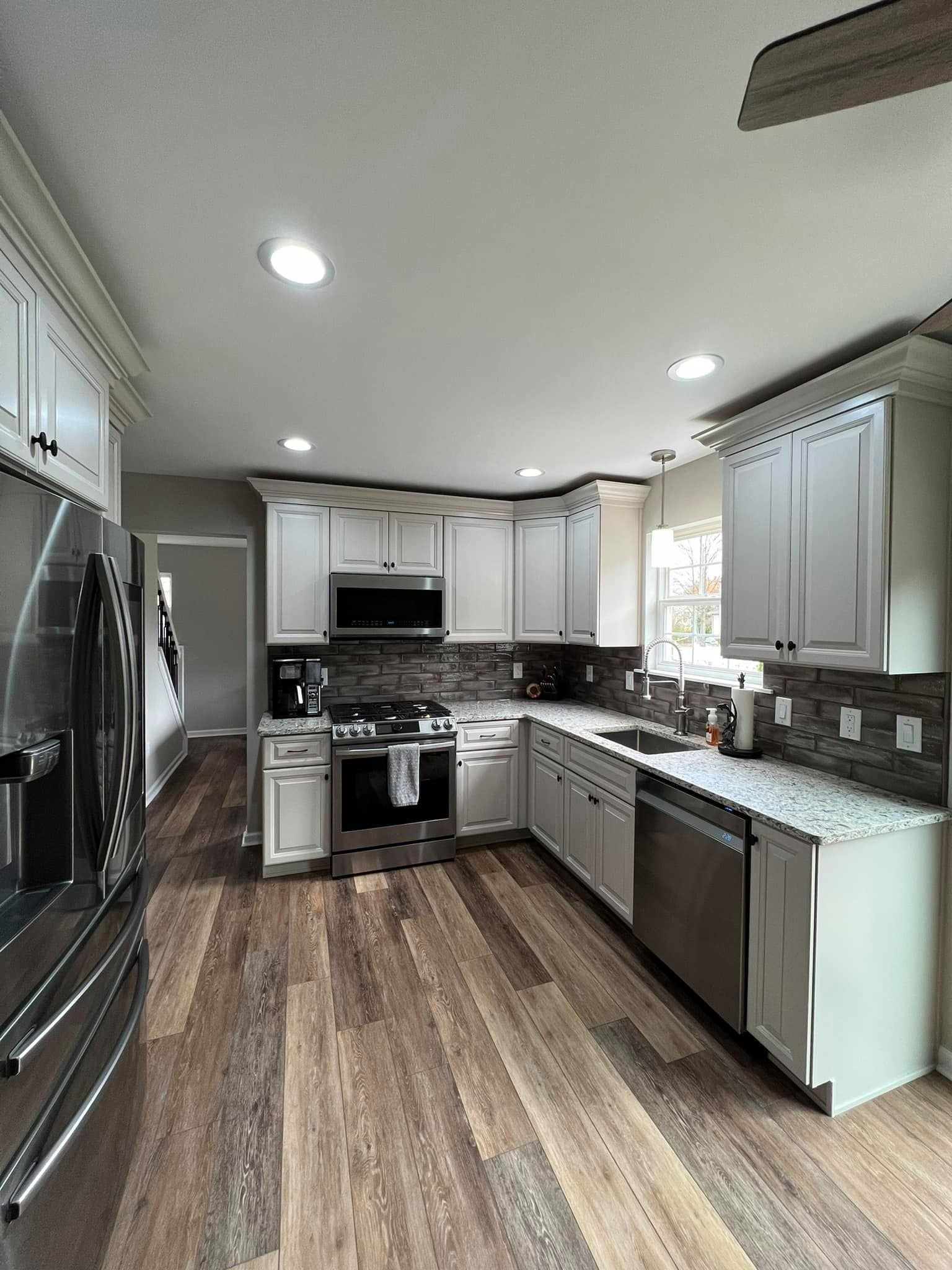 A kitchen with white cabinets , stainless steel appliances , and hardwood floors.