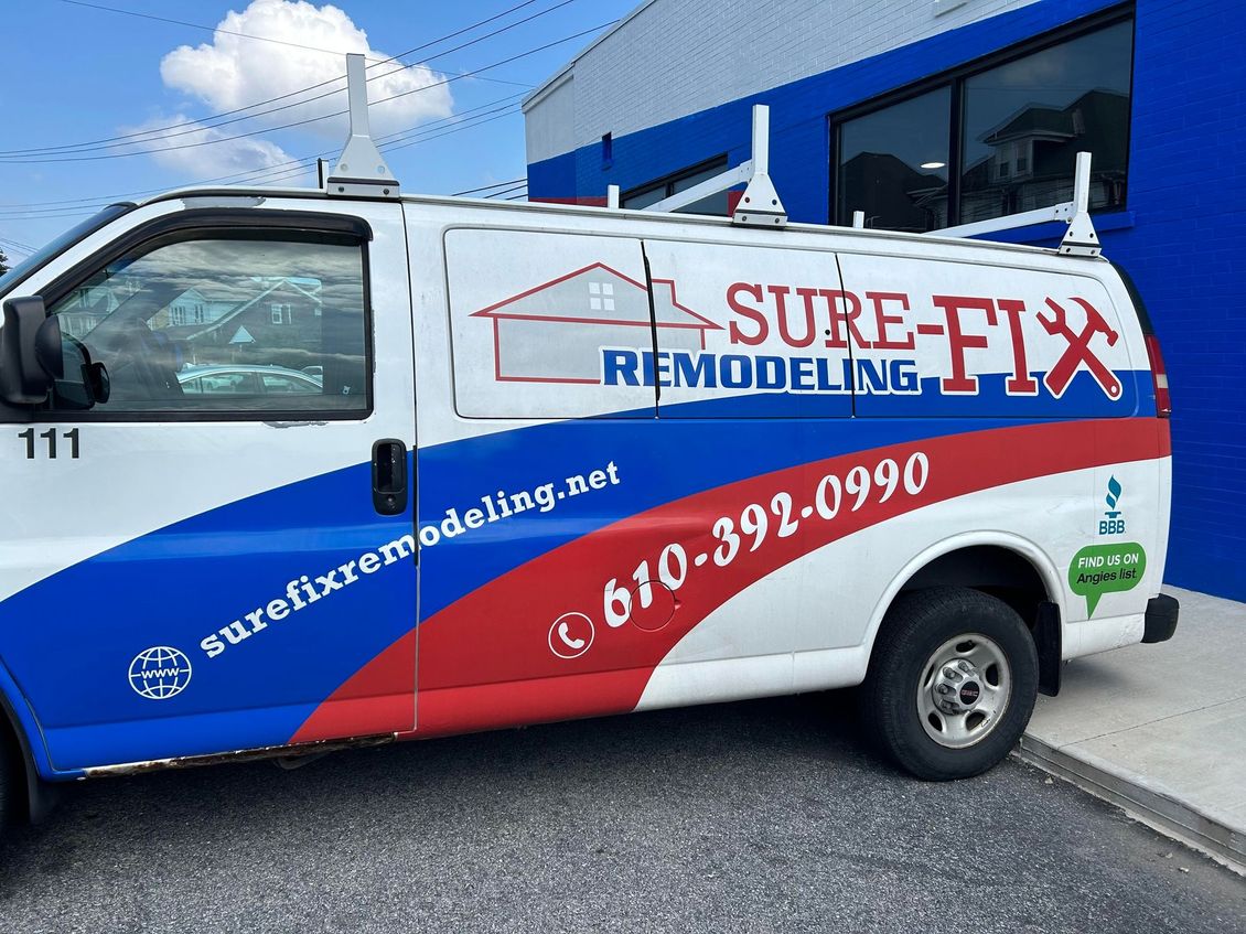 A sure-fix remodeling van is parked in front of a blue building