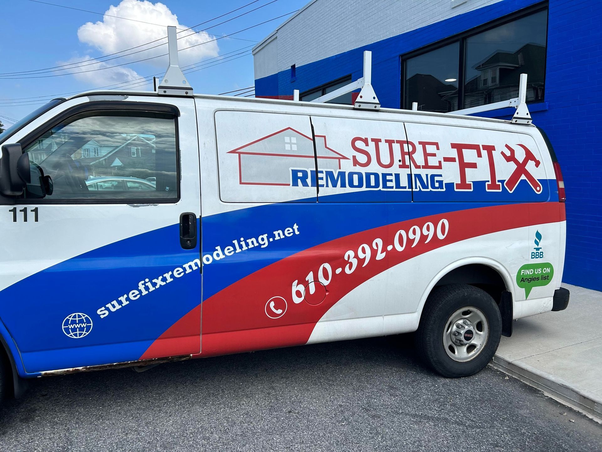 A sure-fix remodeling van is parked in front of a blue building