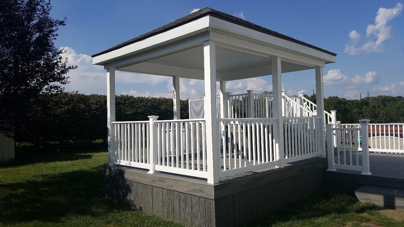 A white gazebo with a white railing in a backyard