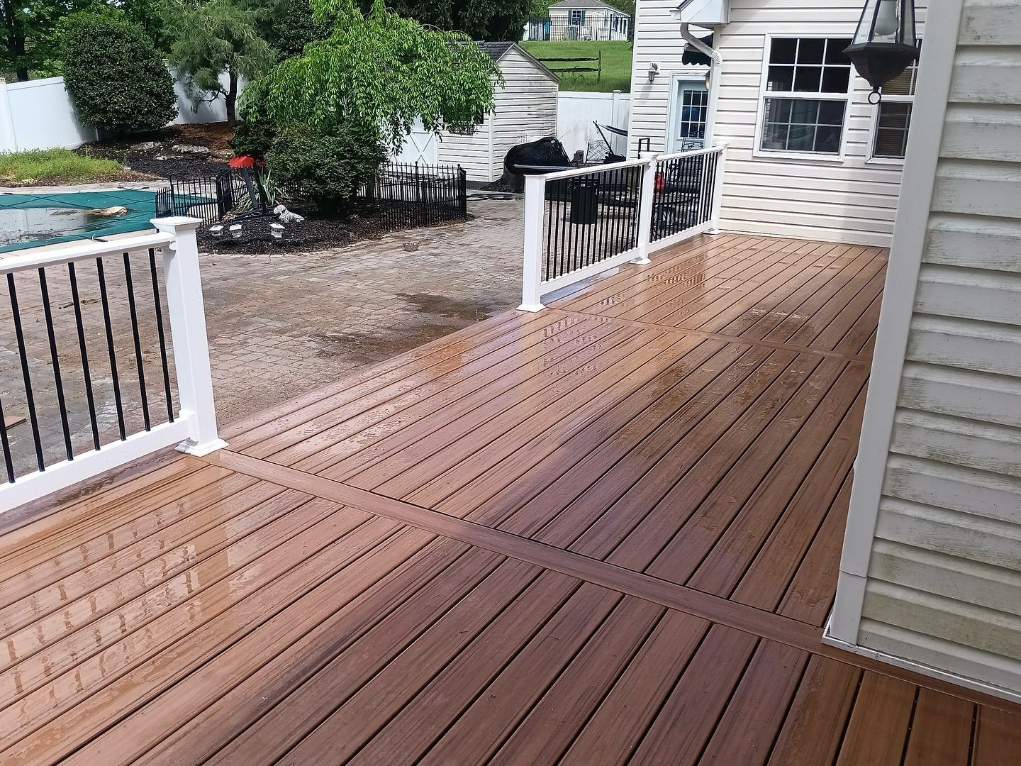 A wooden deck with a white railing and a pool in the background.