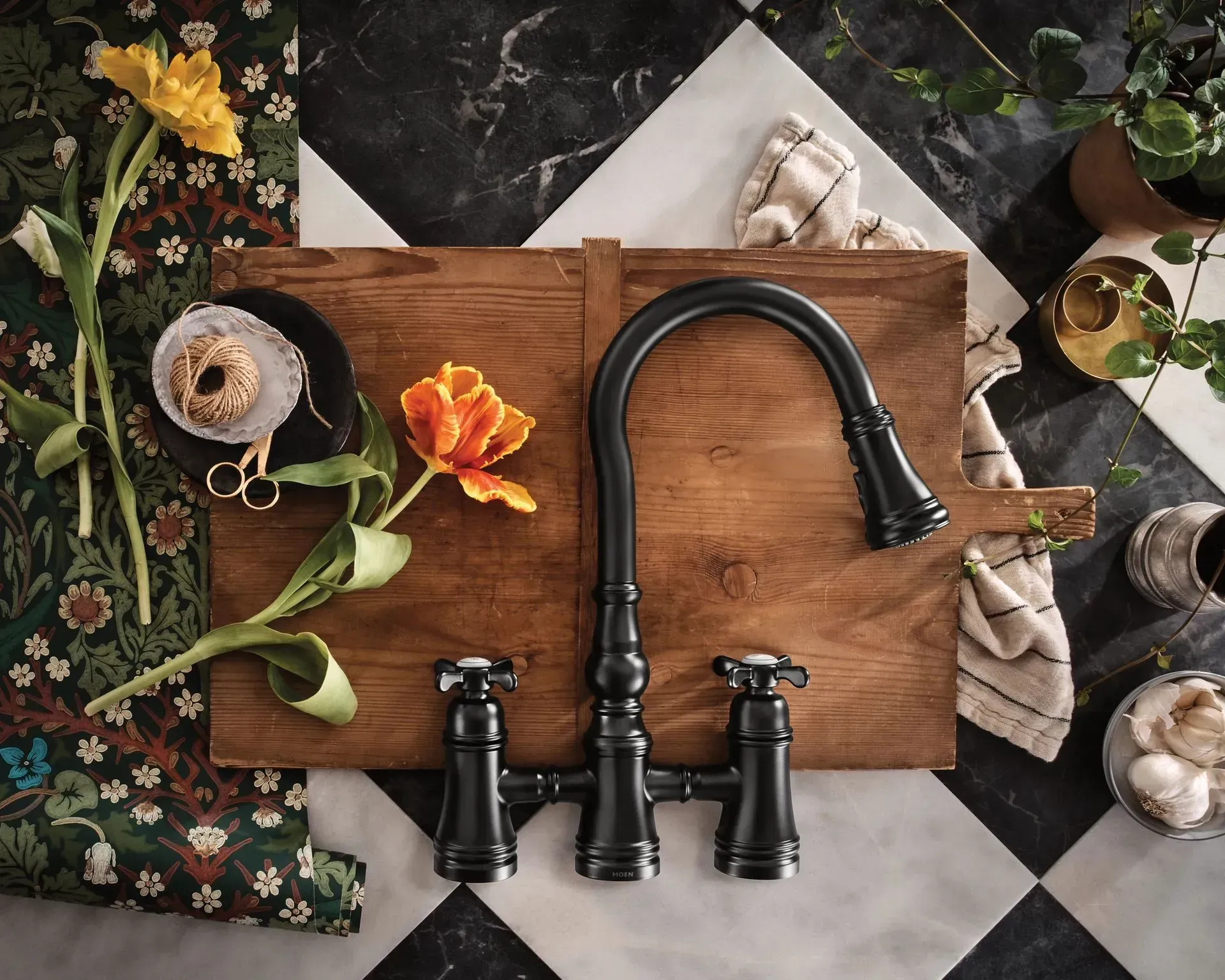 A black faucet is sitting on a wooden cutting board surrounded by flowers.