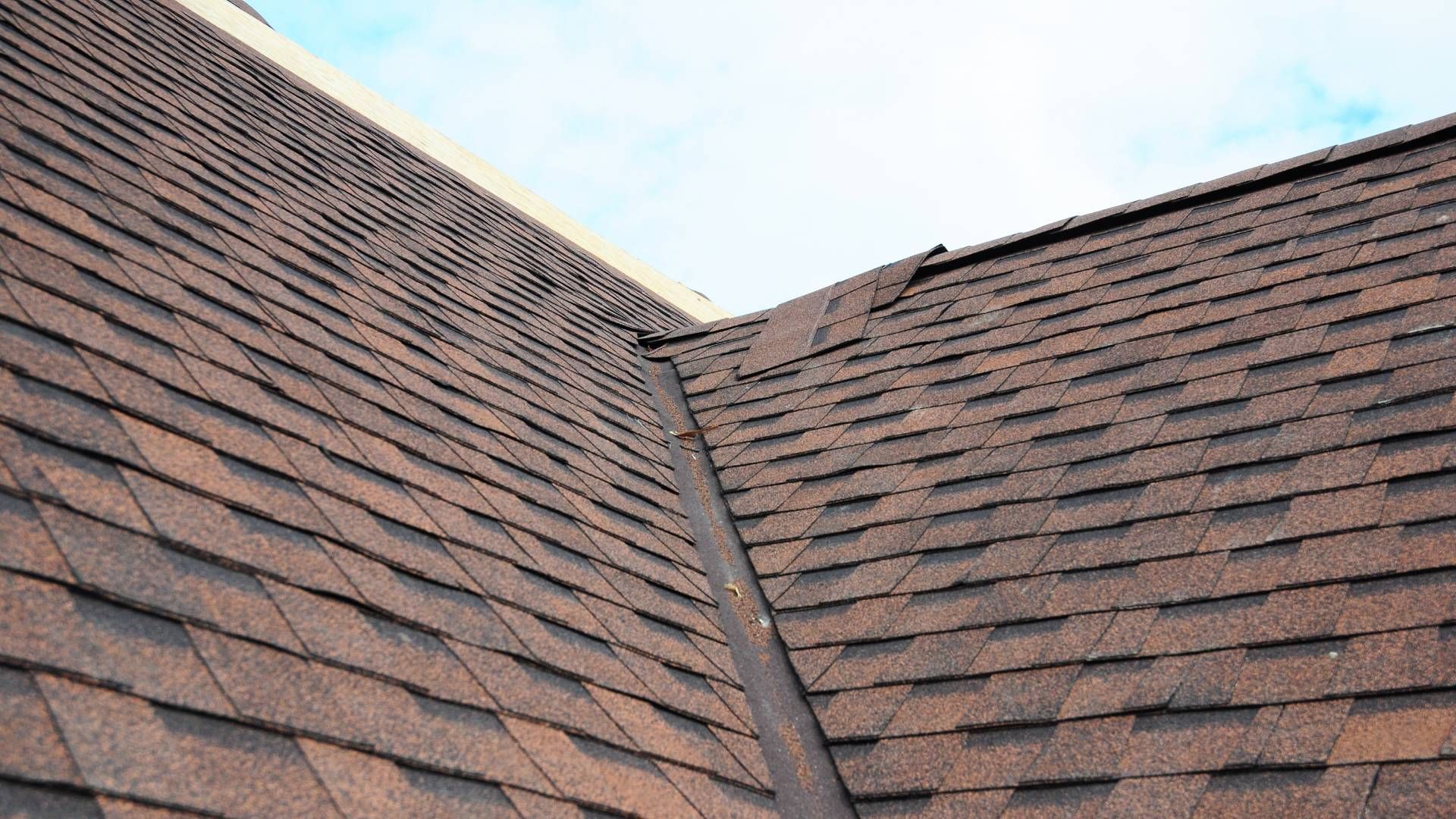 A close up of a roof with brown shingles and a blue sky in the background.