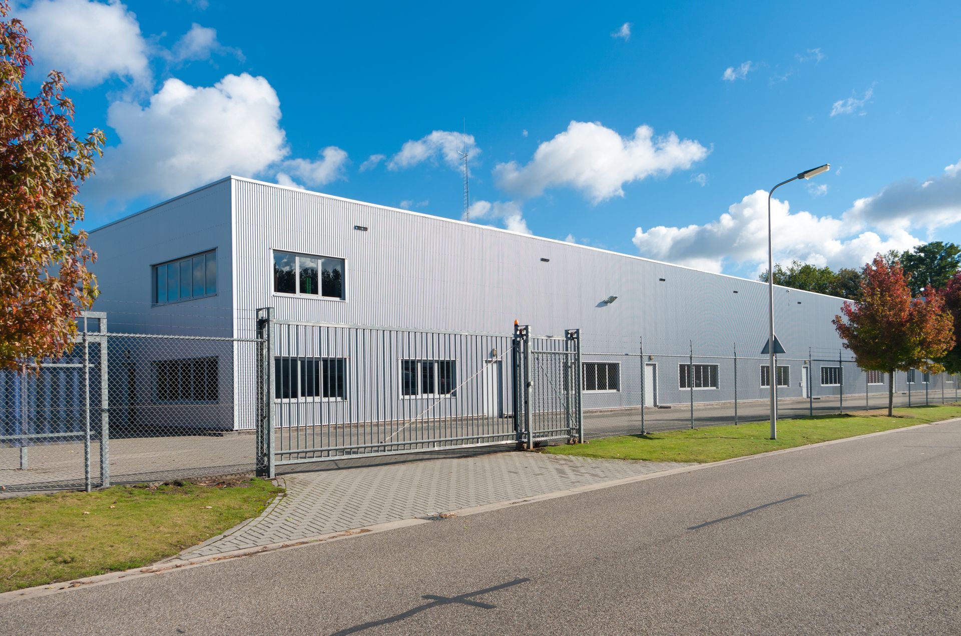 A gated industrial building surrounded by foliage and cloudy blue skies. 