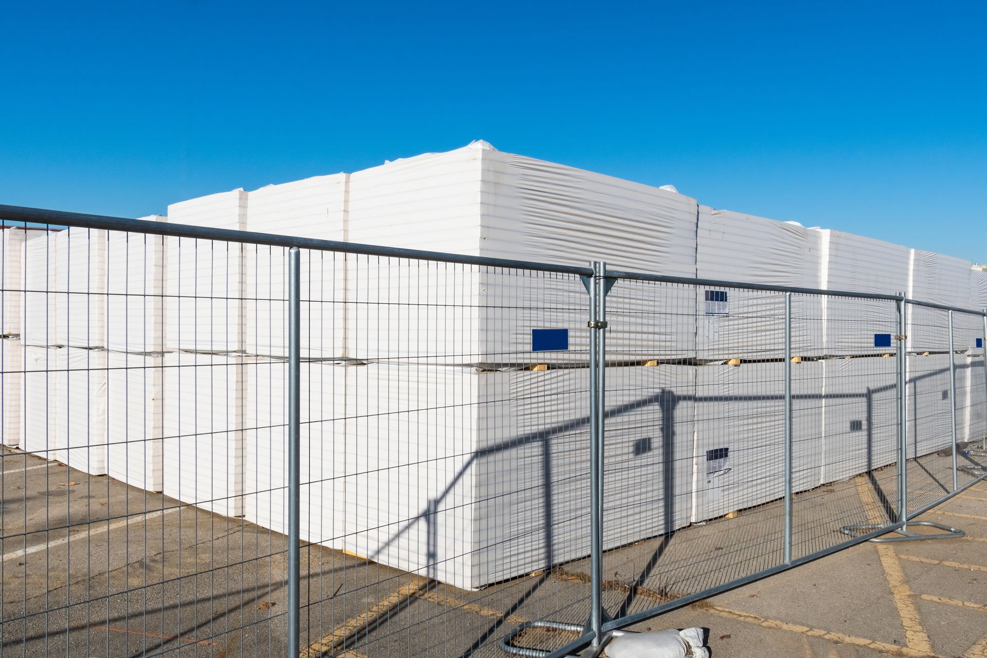 Stacks of sheetrock outside a commercial construction job surrounded by fencing. 