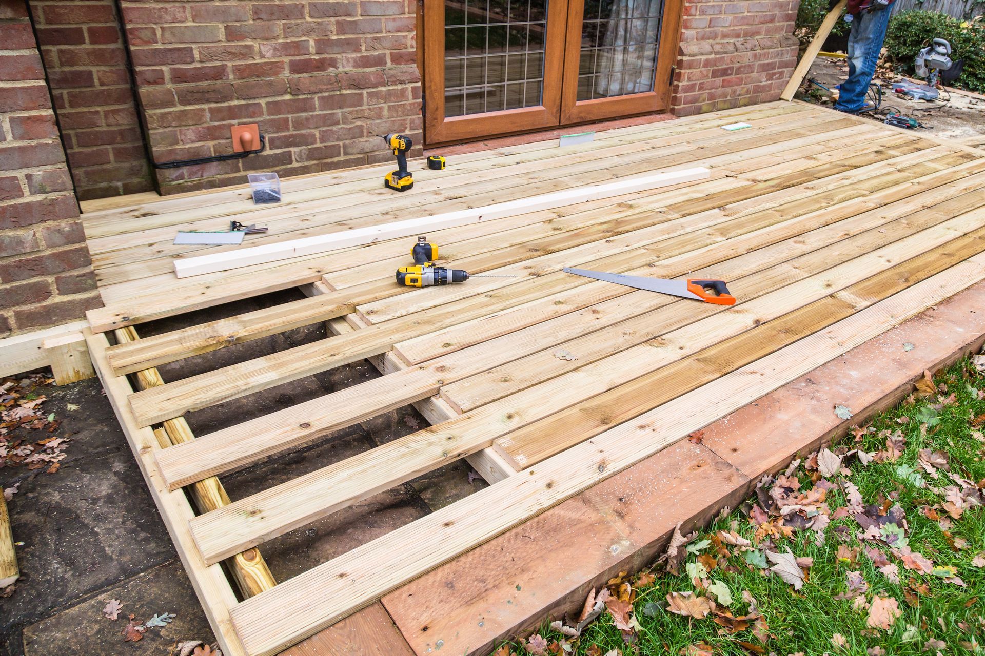 Partially built wooden deck beside a brick house, with tools and open joists visible