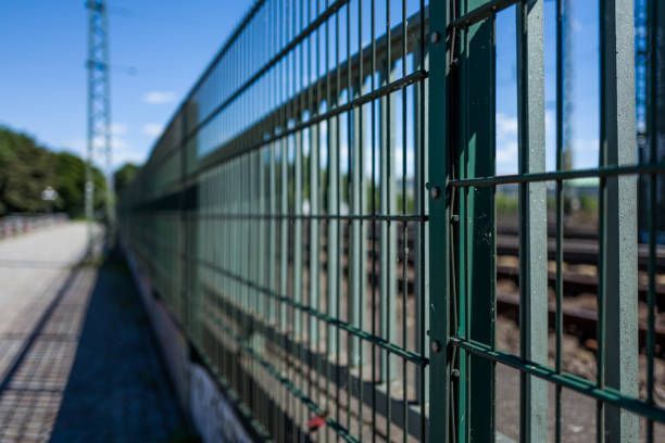 A green fence is surrounding a train track.