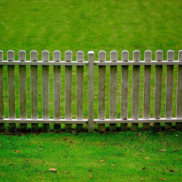 A white picket fence surrounds a lush green field.