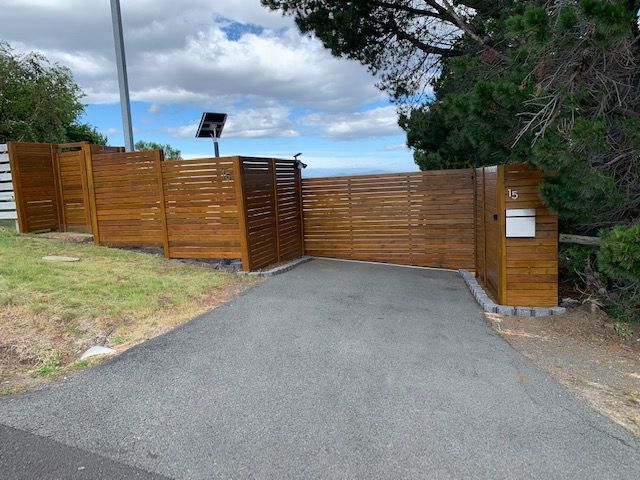 A wooden fence surrounds a driveway leading to a house.