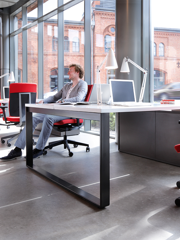 A man sits at a desk in front of a large window
