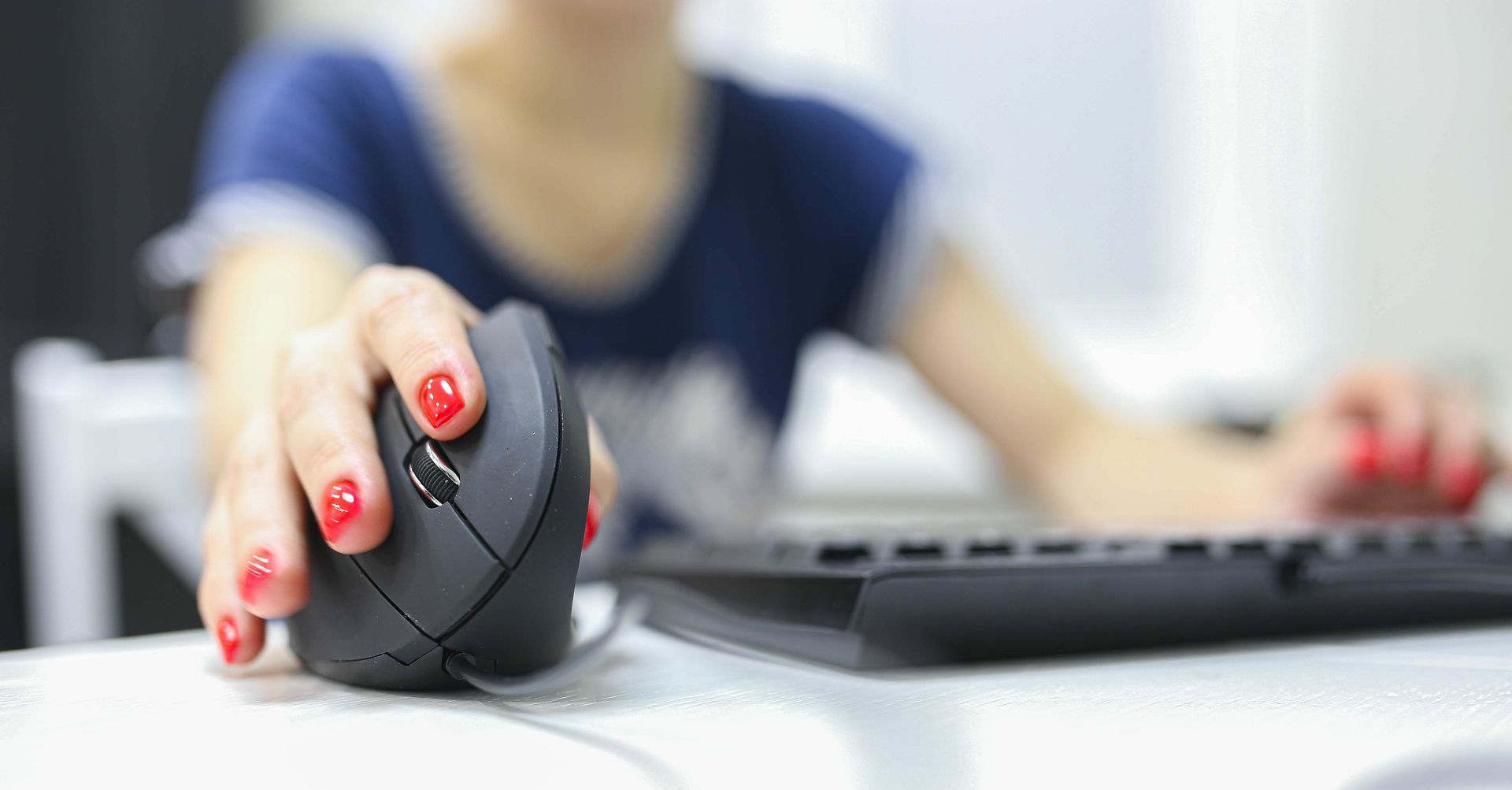 A woman with red nails is using a computer mouse and keyboard.