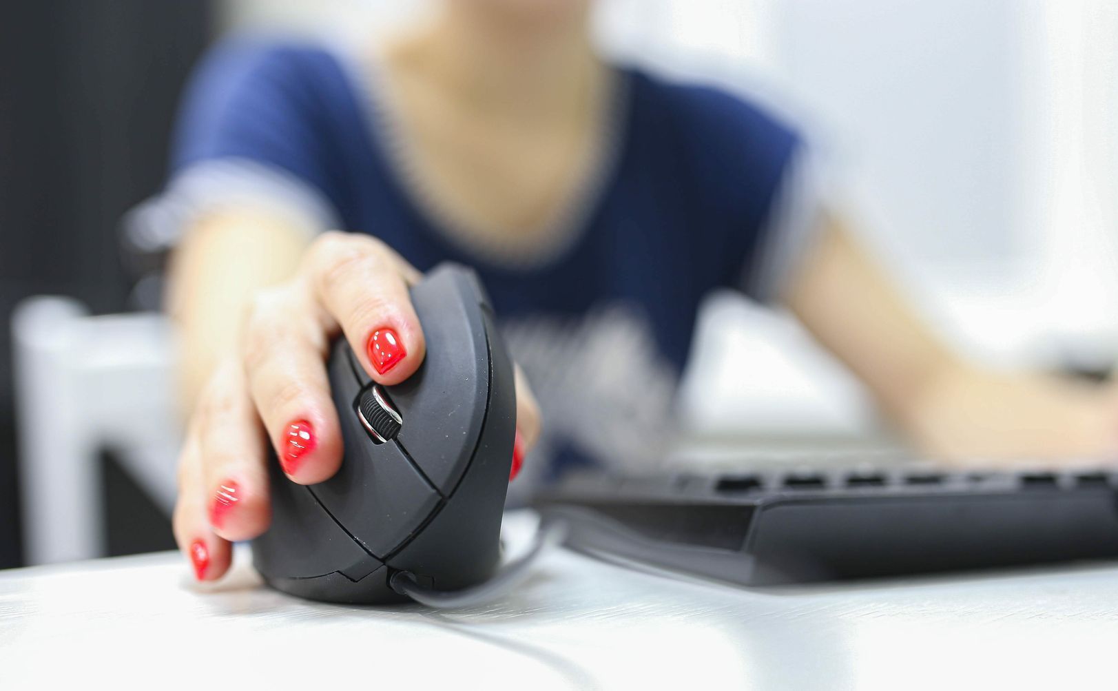 A woman is sitting at a desk using a computer mouse.