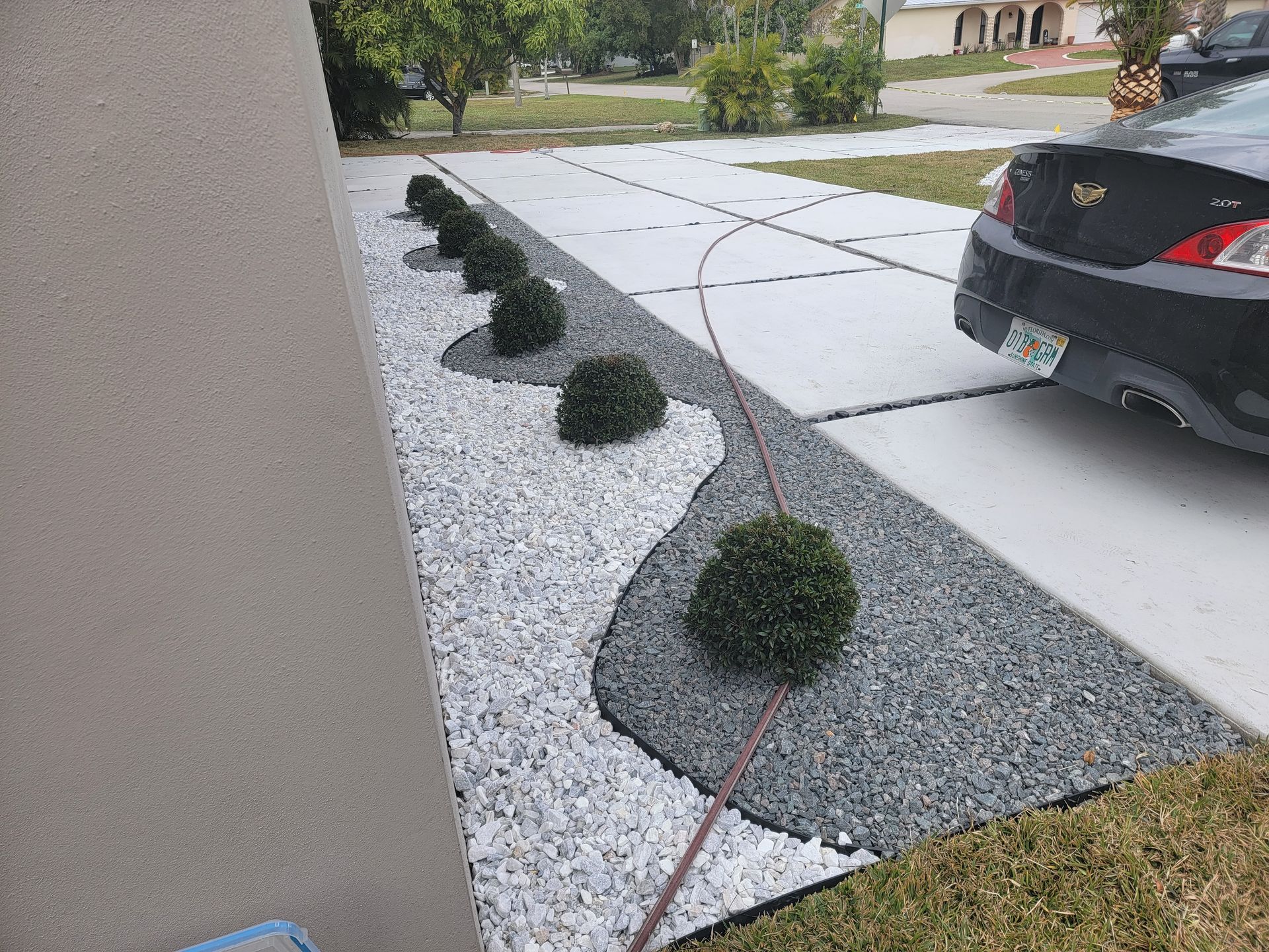 A black car is parked in a driveway next to a garden.
