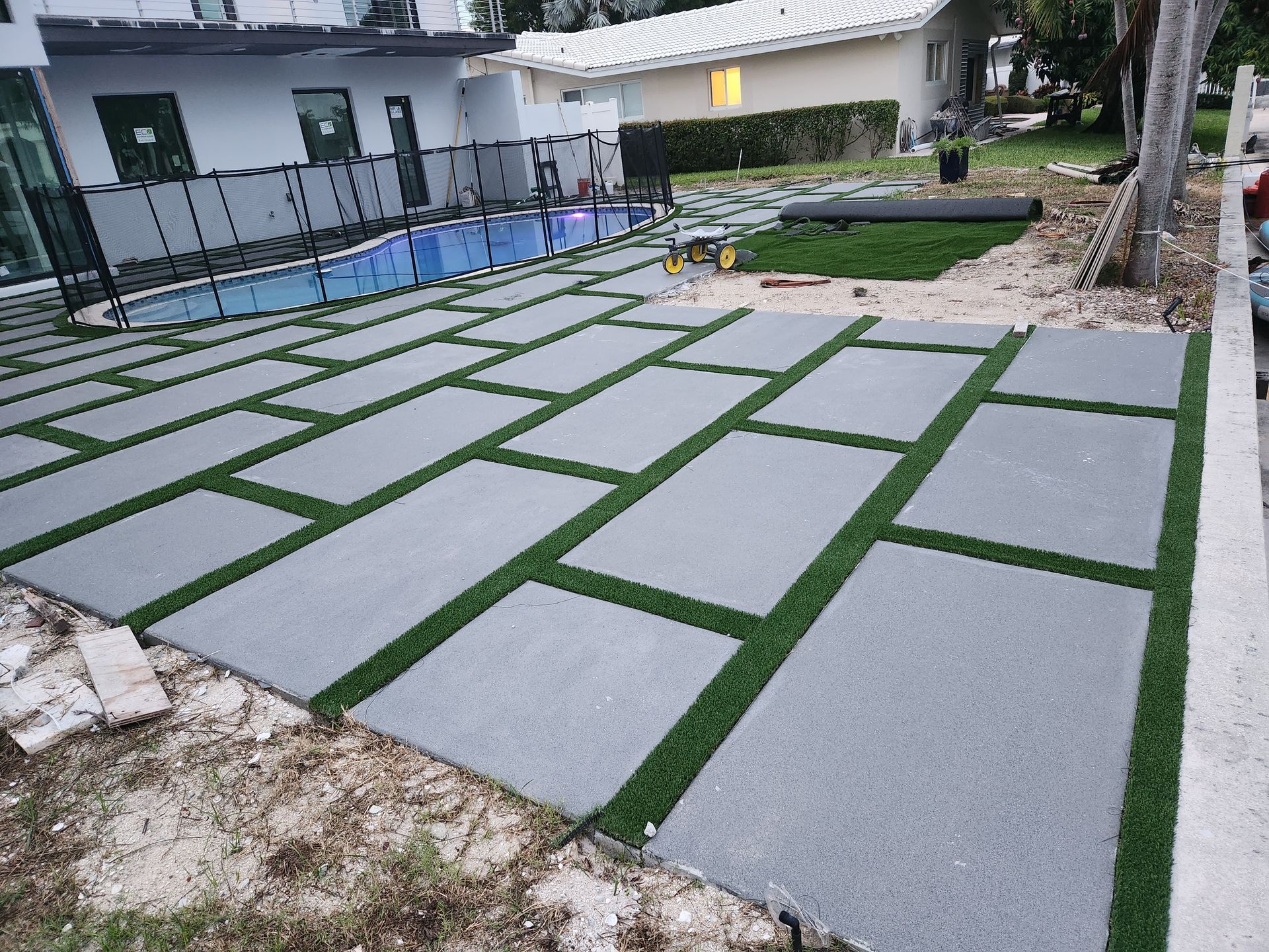 A patio with artificial grass and a pool in the background.
