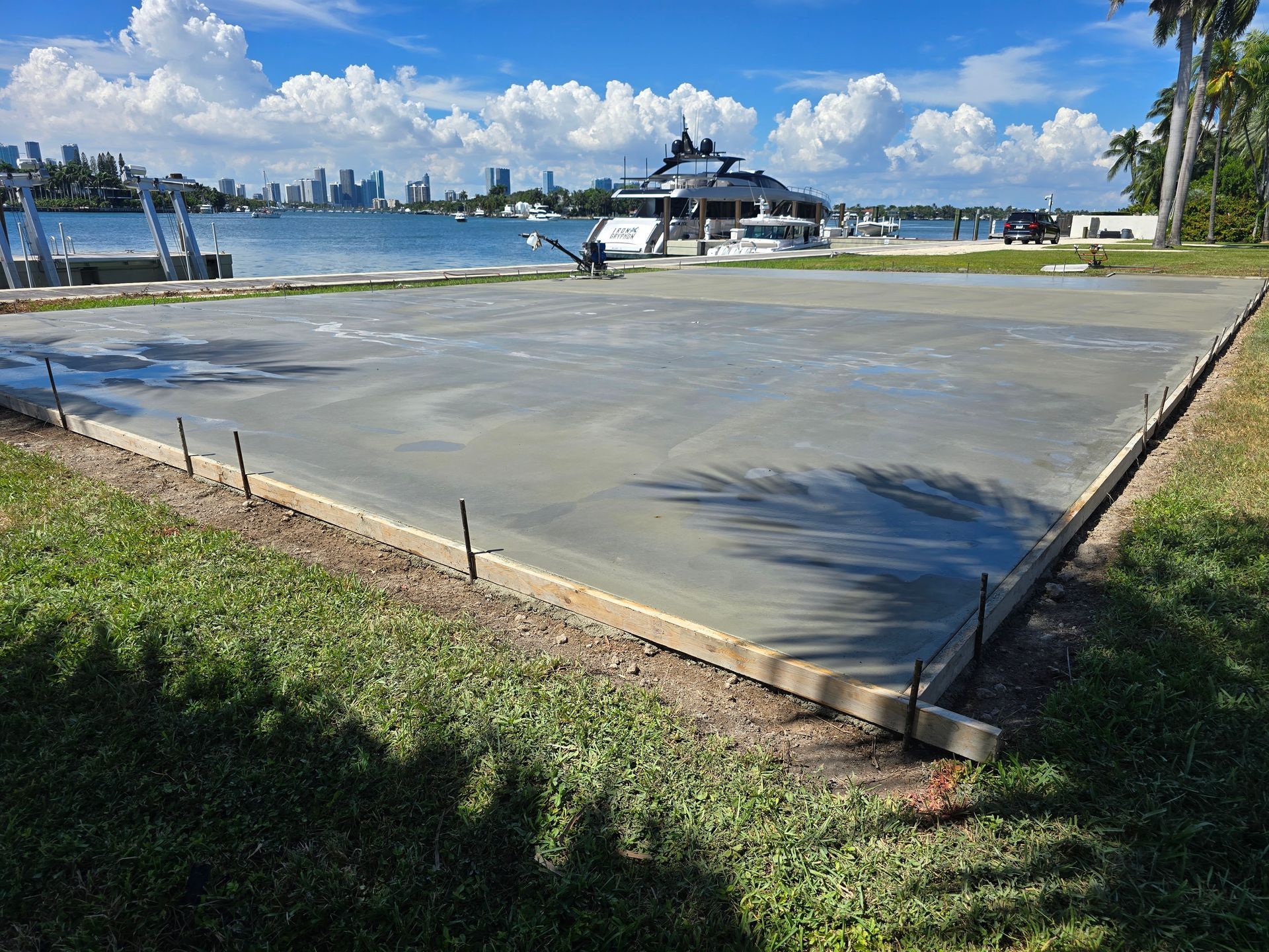 A Concrete Driveway Is Being Built Next to A Body of Water with A Boat in The Background.
