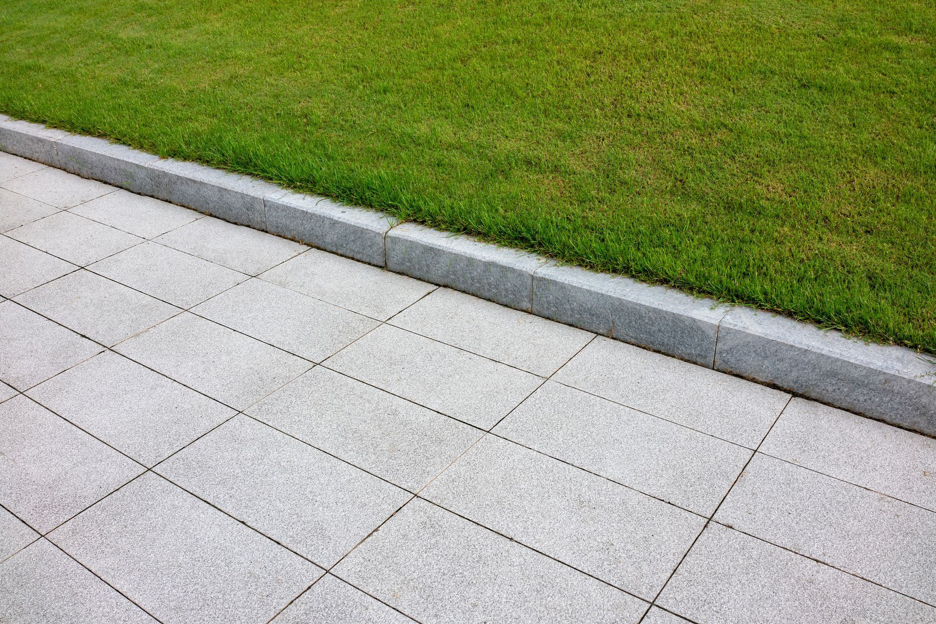 A sidewalk with a curb and grass on the side of it.