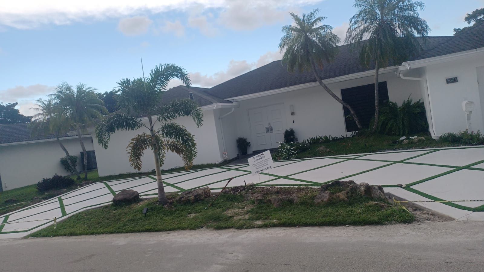 A white house with a large driveway and palm trees in front of it.