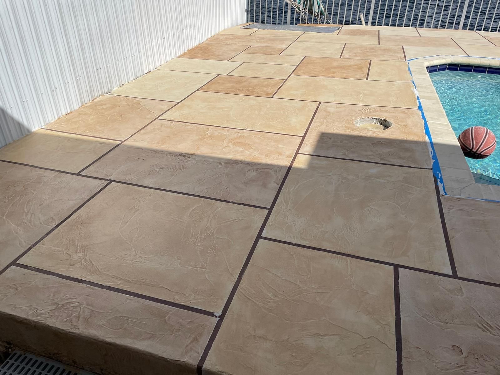 A basketball is sitting on the side of a concrete patio next to a pool.