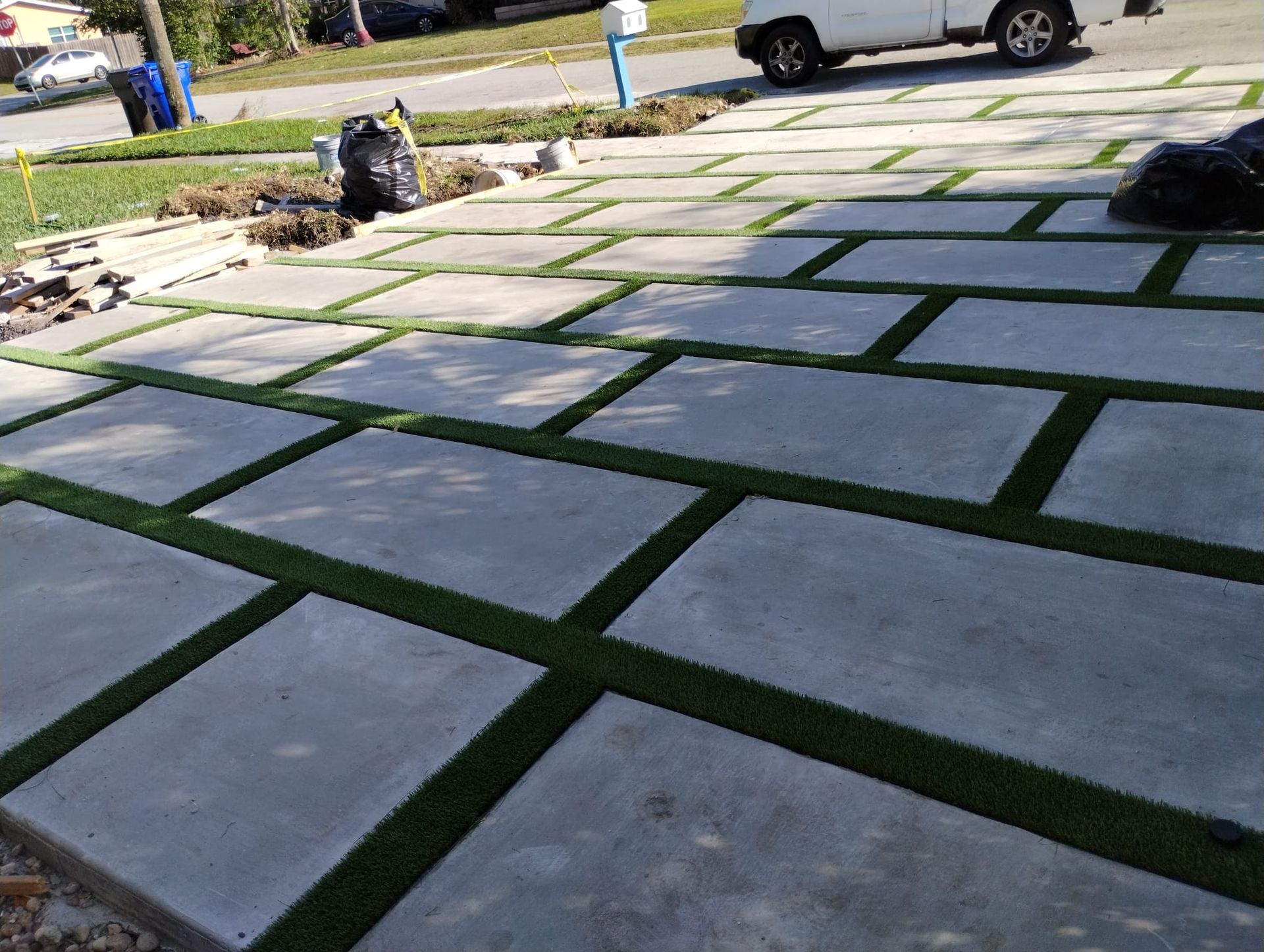 A white truck is parked on a concrete driveway with grass growing out of it.