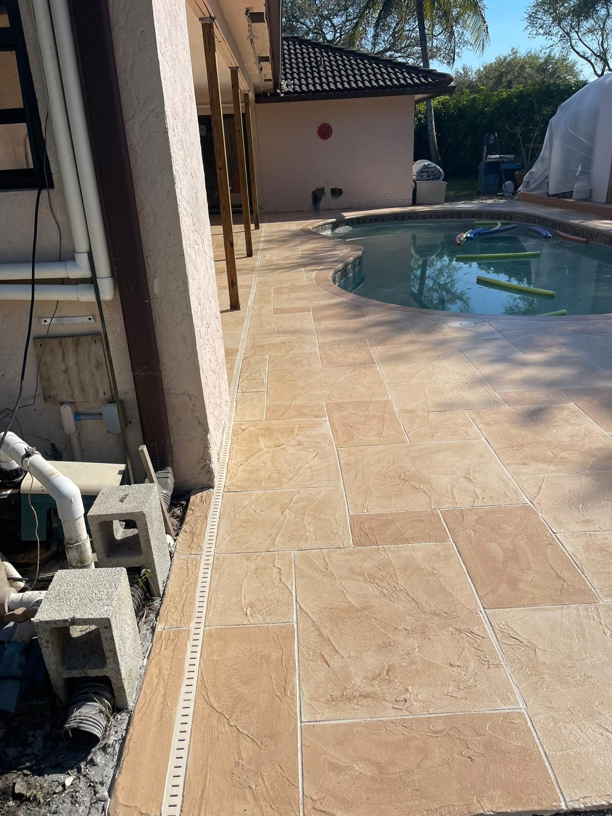 A Tiled Walkway Leading to A Swimming Pool with A House in The Background.
