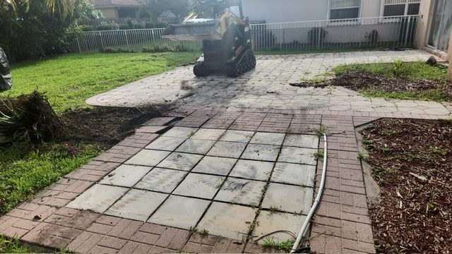 A car is driving down a brick driveway next to a house.