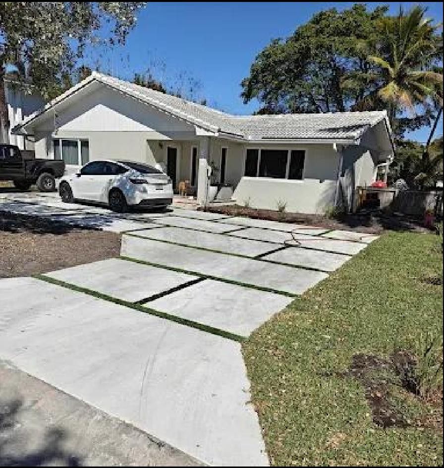 A white house with a modern concrete driveway. A white car sits in the driveway, with green grass lining the edge.