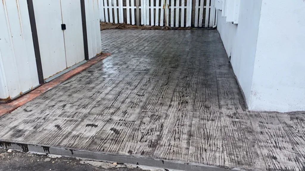 A concrete driveway with a white fence in the background.