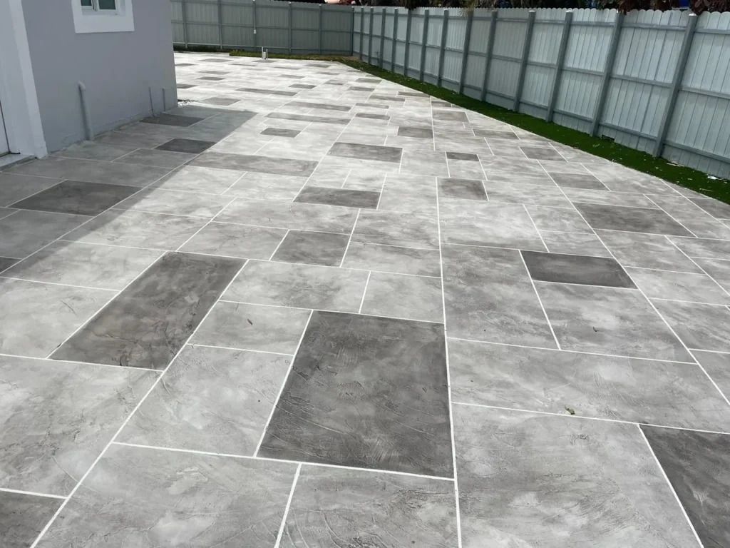 A gray tiled driveway with a white fence in the background.