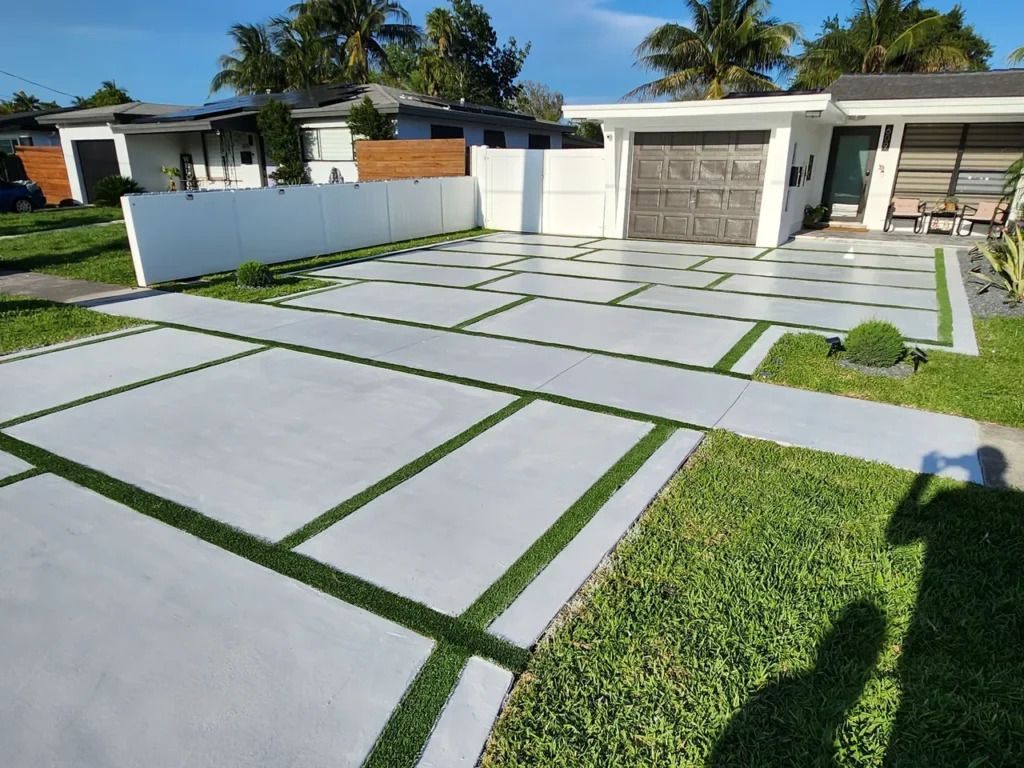 A concrete driveway with grass growing out of it in front of a house.