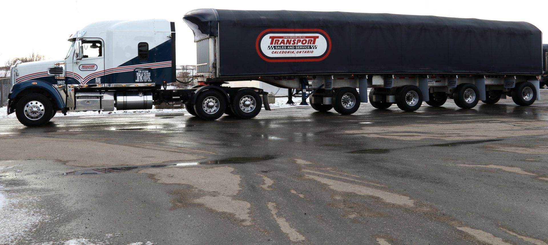 A semi truck is parked in a parking lot with a black tarp on the side.