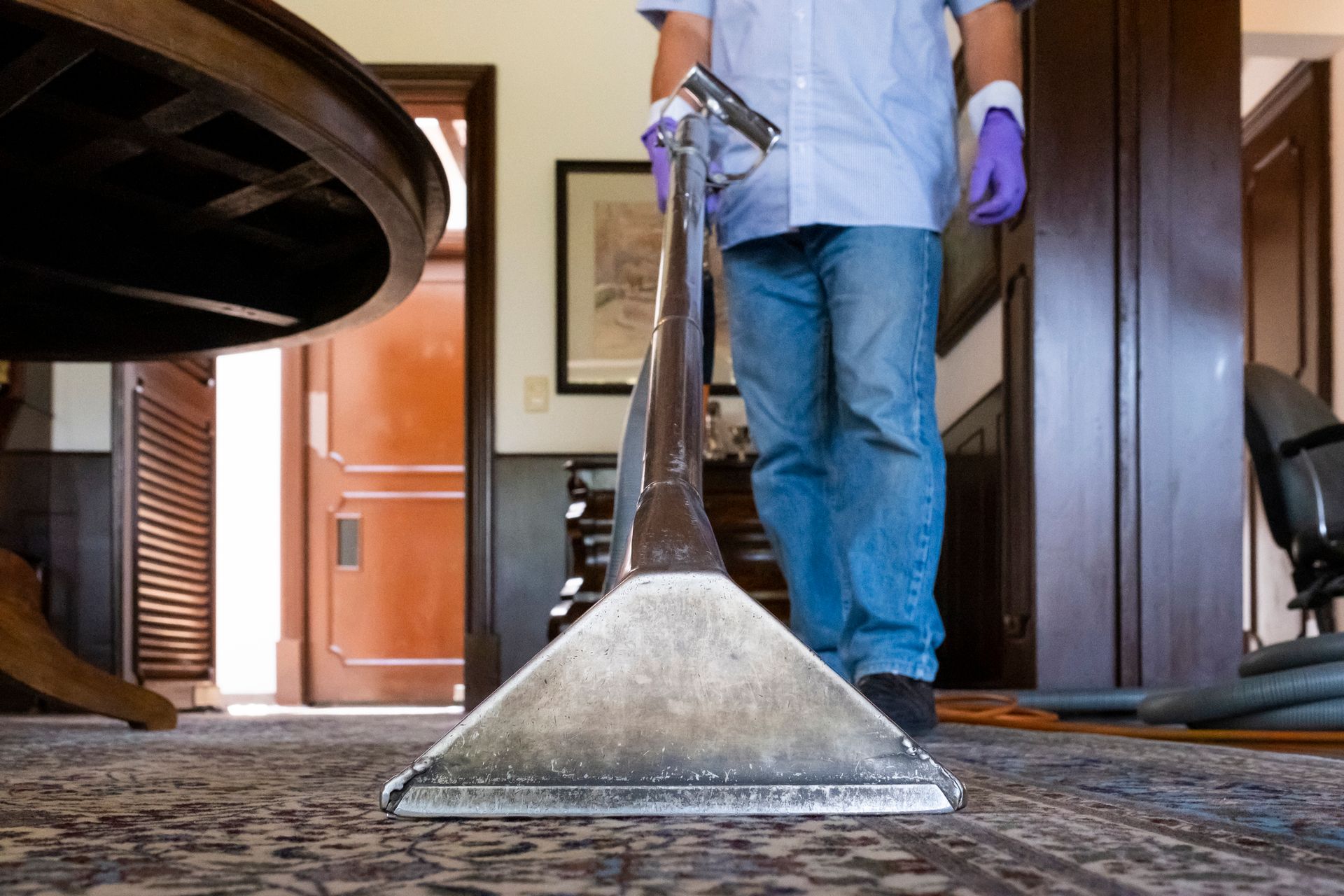 Janitor cleaning a carpet using a vacuum cleaner, showcasing expert carpet cleaning tecniques.