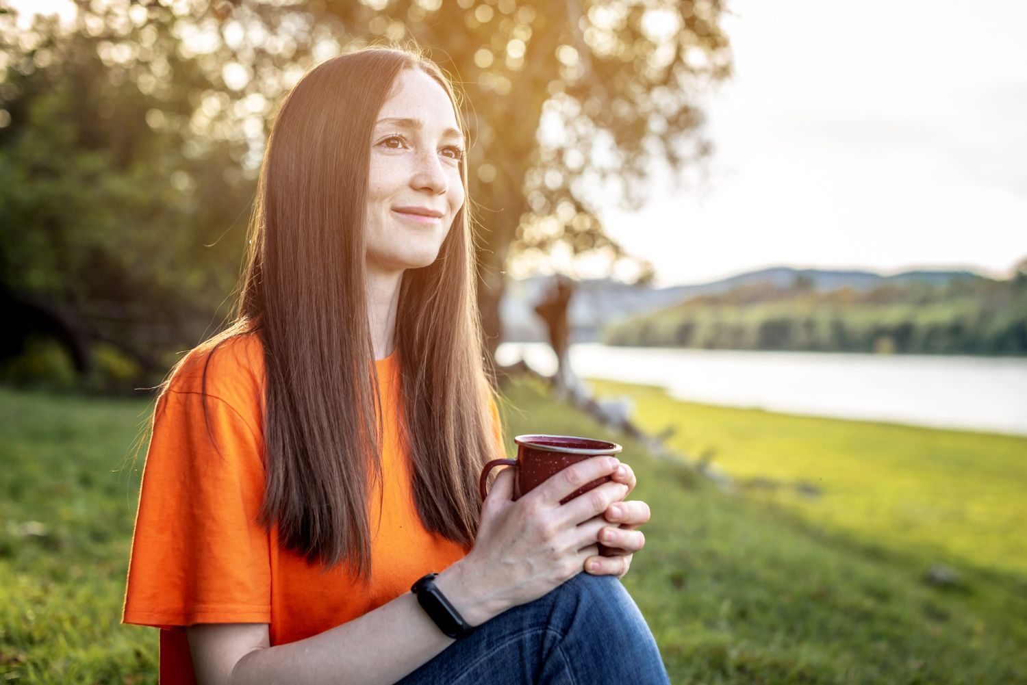 A woman is sitting on the grass holding a cup of coffee.