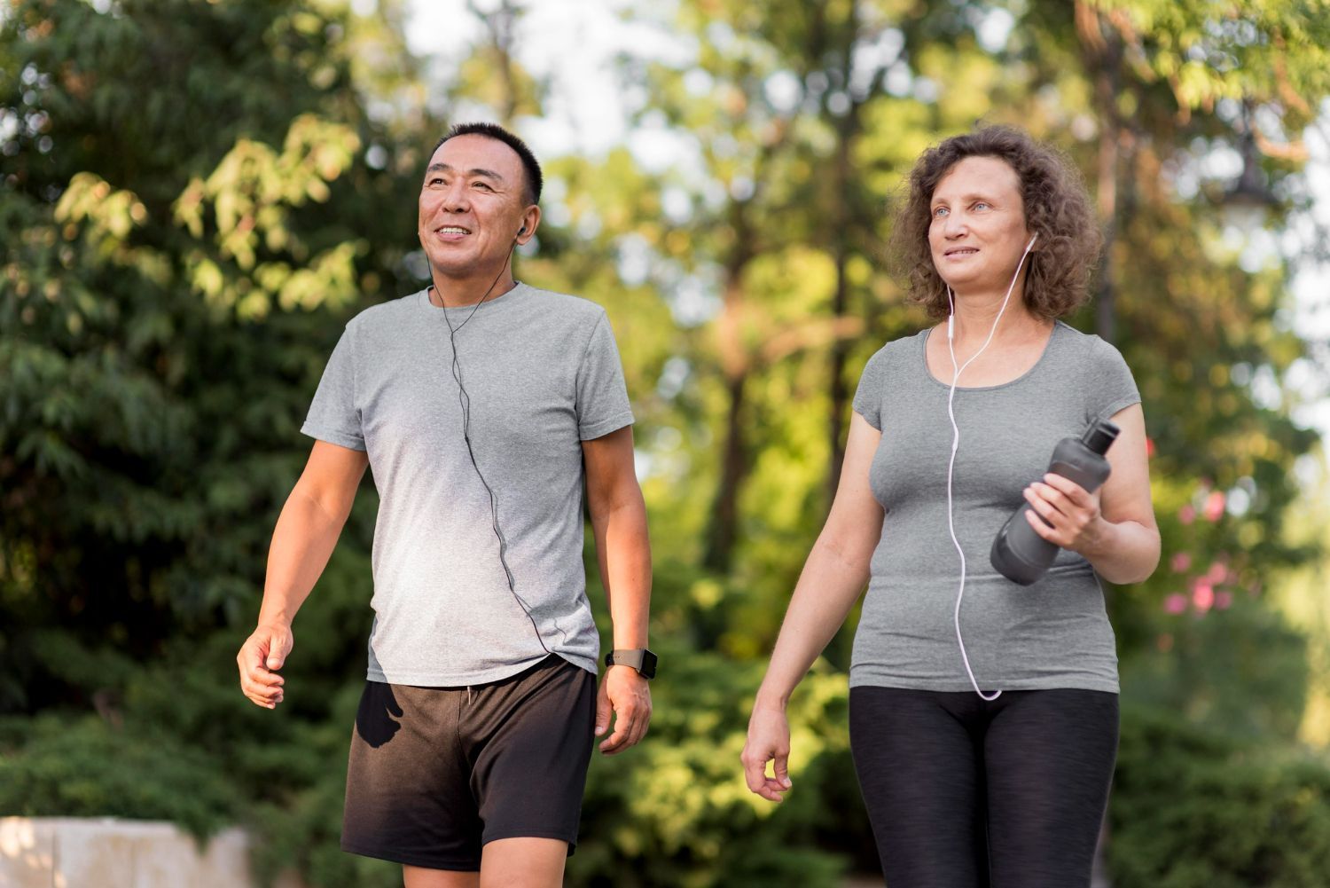 Two people walking outdoors, one holding water bottle, both wearing gray shirts.