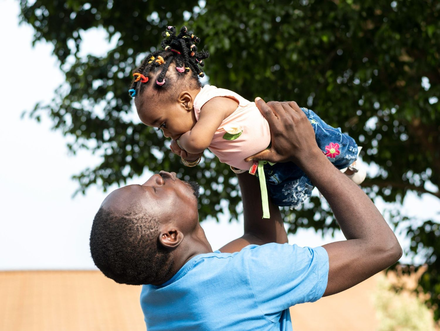 Man holding a baby up in the air; sunny outdoor setting.
