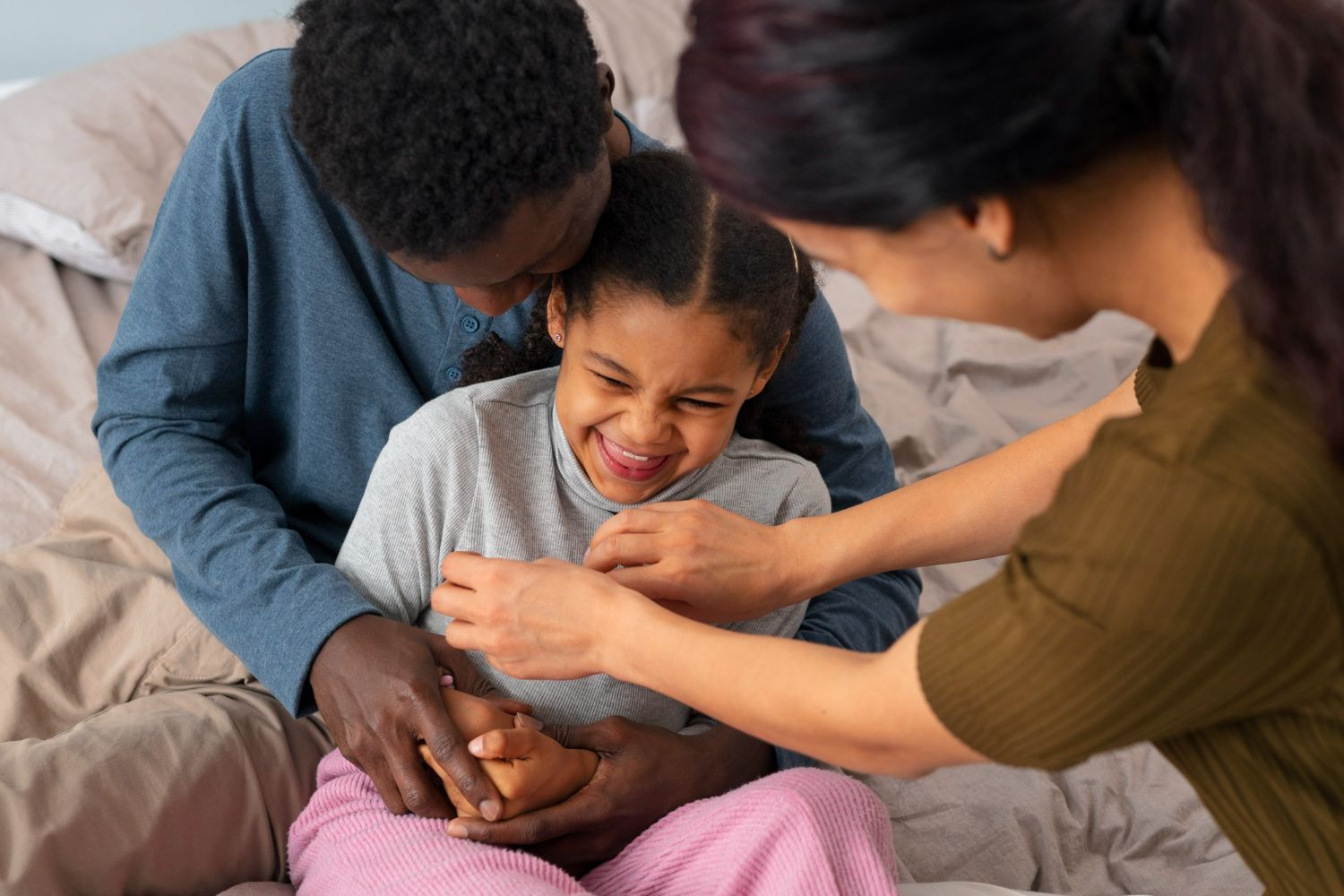 Family tickling and laughing on a bed.