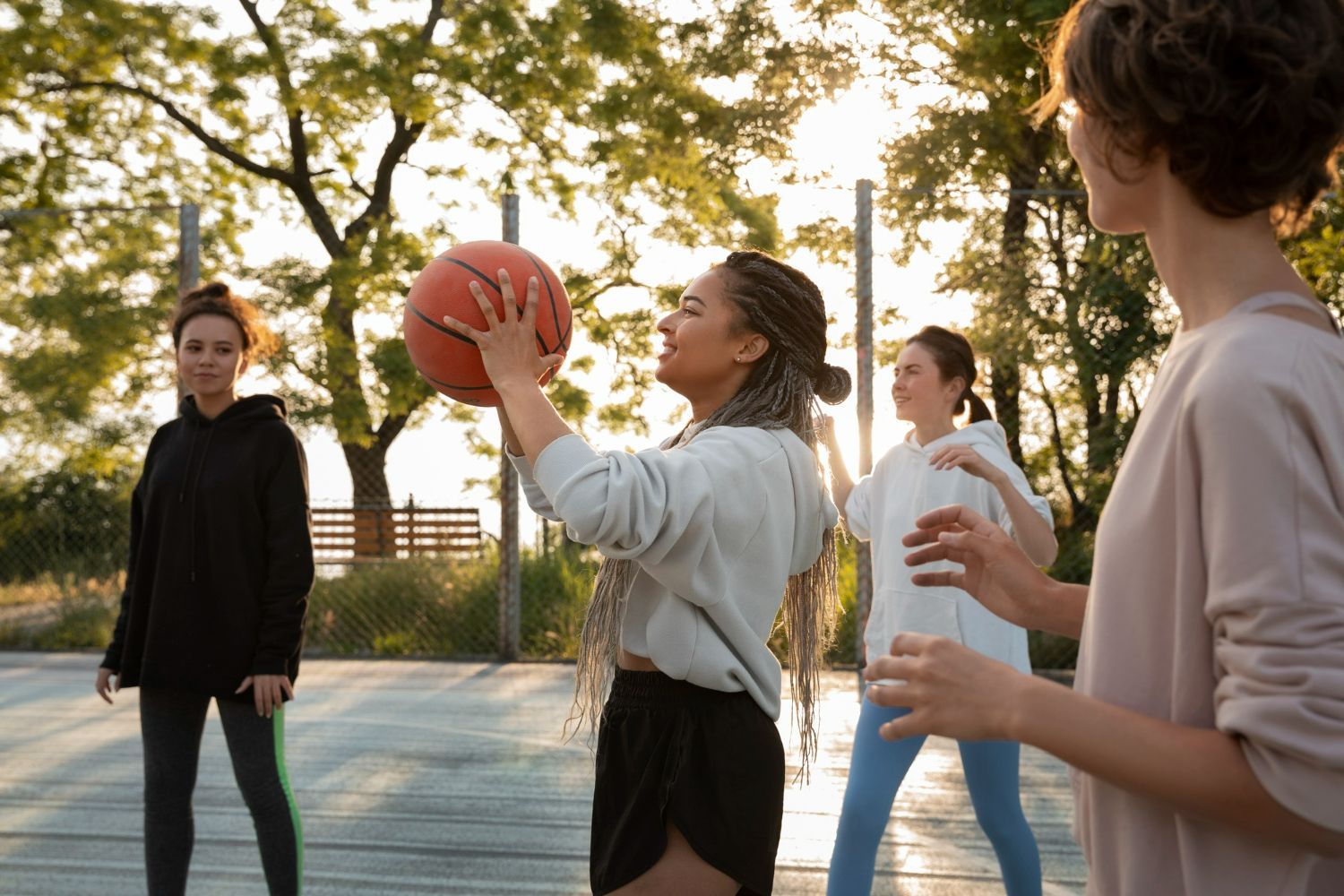 People playing basketball on an outdoor court. One person holding ball, others watching.
