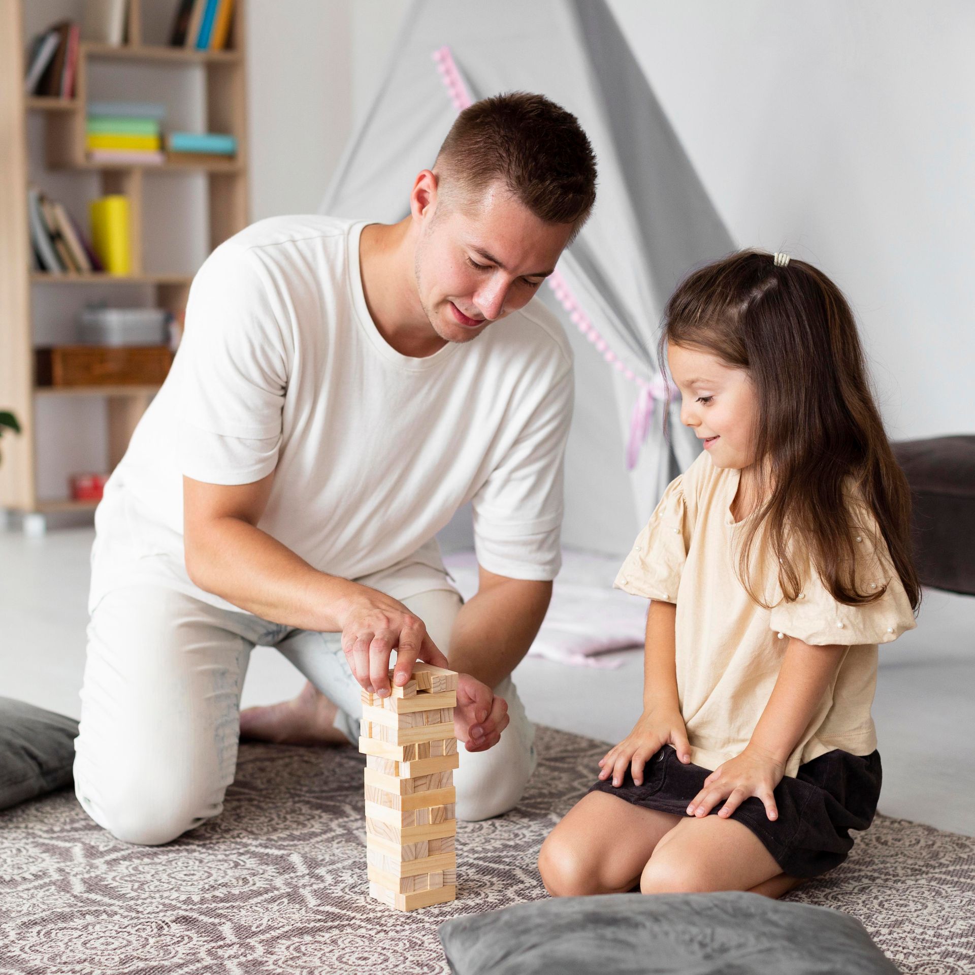 A man and a little girl are playing jenga on the floor.