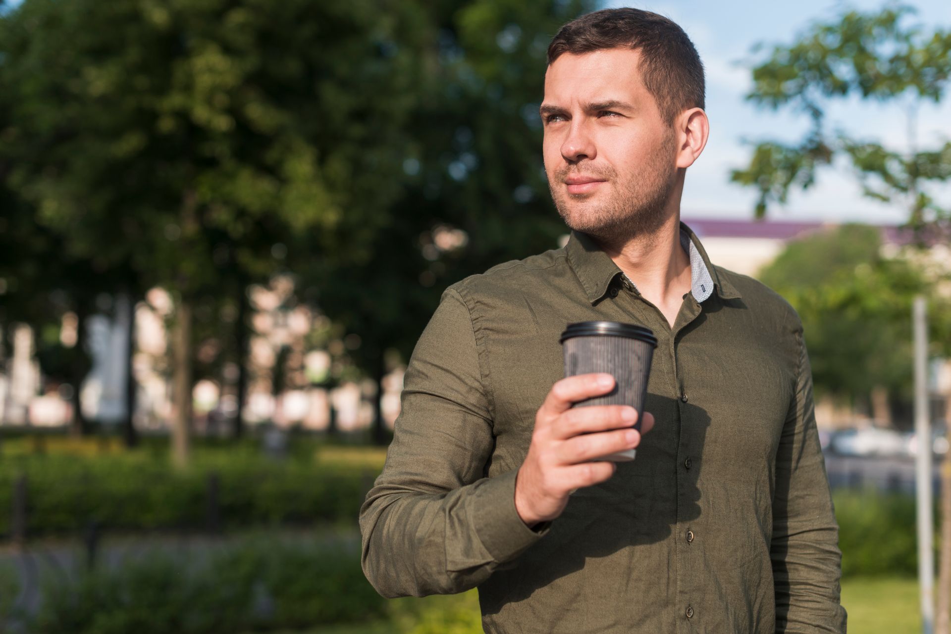 A man in a green shirt is holding a cup of coffee in a park.