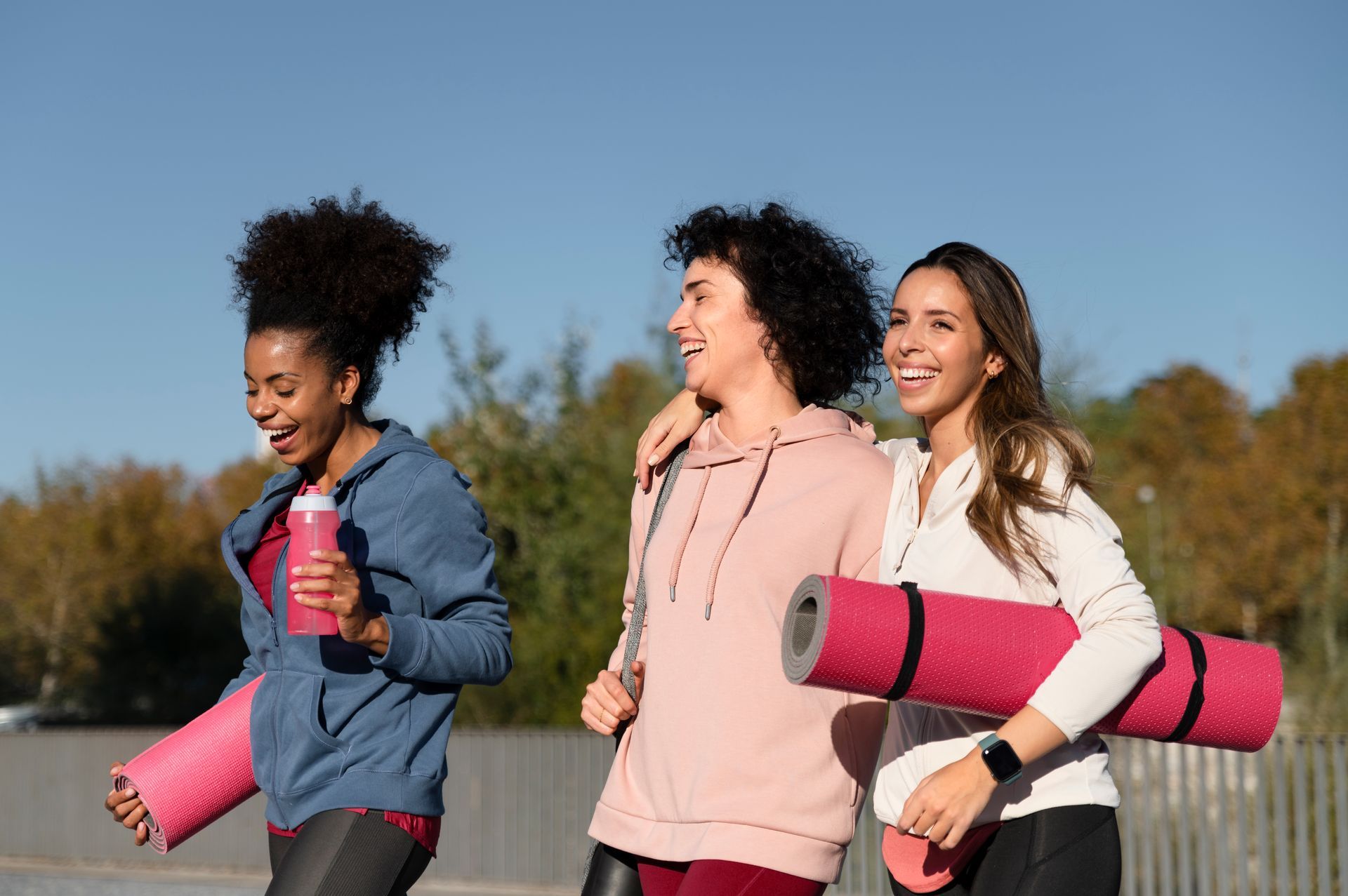 Three women are walking with yoga mats and water bottles.