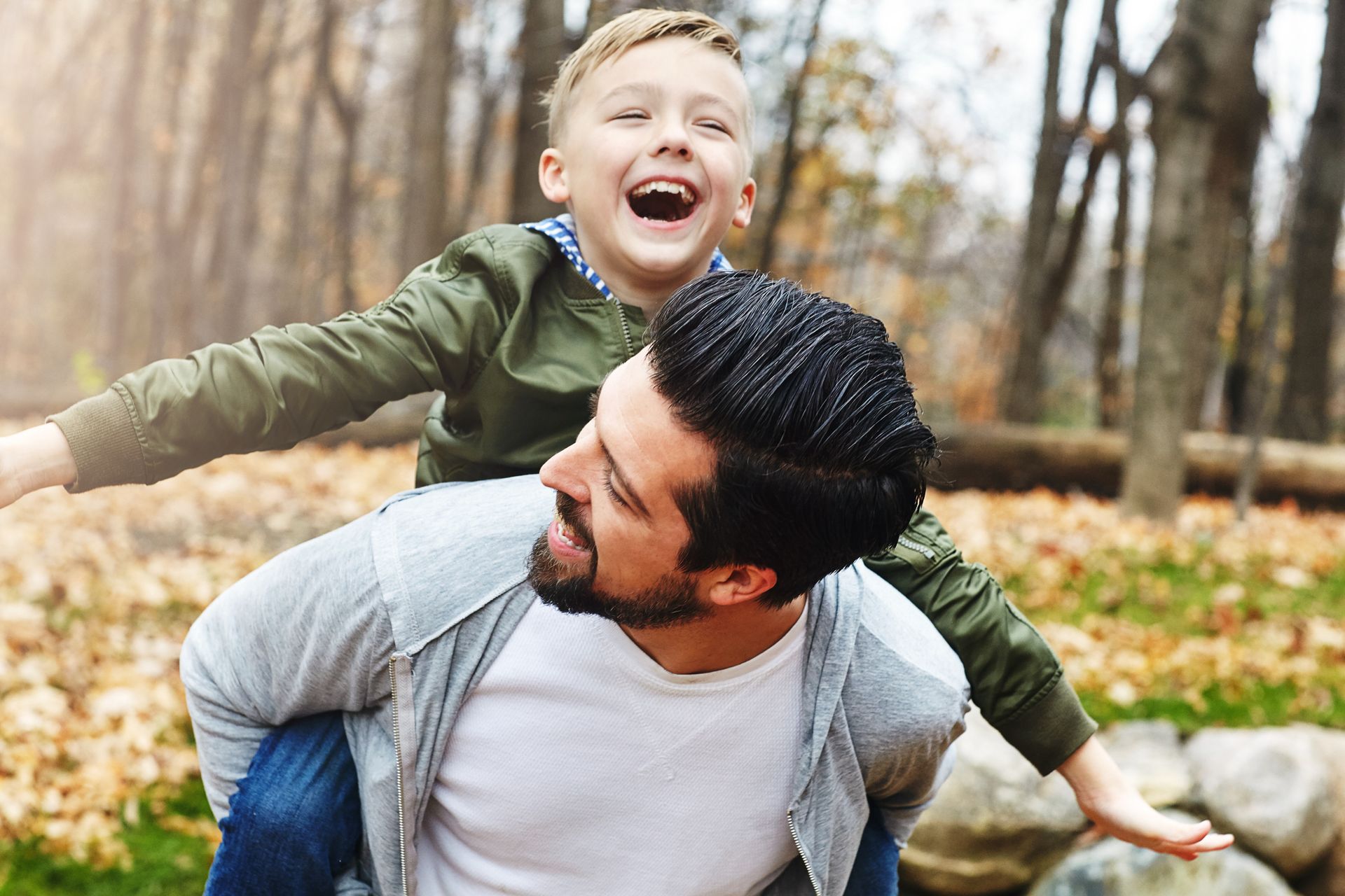 A man is carrying a young boy on his shoulders in the woods.