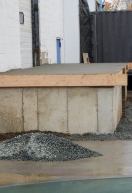 Concrete loading dock with fresh concrete surface, wooden edge, and pile of gravel.