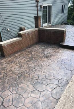 Stamped concrete patio with brick wall and steps, near a house with siding.