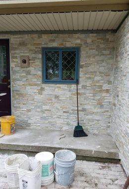 Exterior of a house with stone veneer, blue window, broom, buckets, and concrete porch.