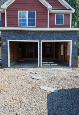 Two-car garage with dark stone facade, red siding above. Gravel driveway in front.