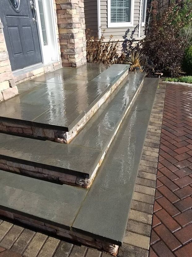 Stone steps leading to a house entrance, wet from rain. Brick walkway on the side.