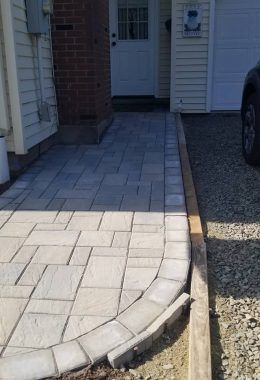 Paved walkway leading to a white door, bordered by stones and wood edging.