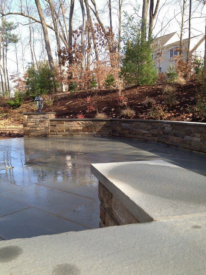 Stone patio with low wall, water reflection, and hillside with trees.
