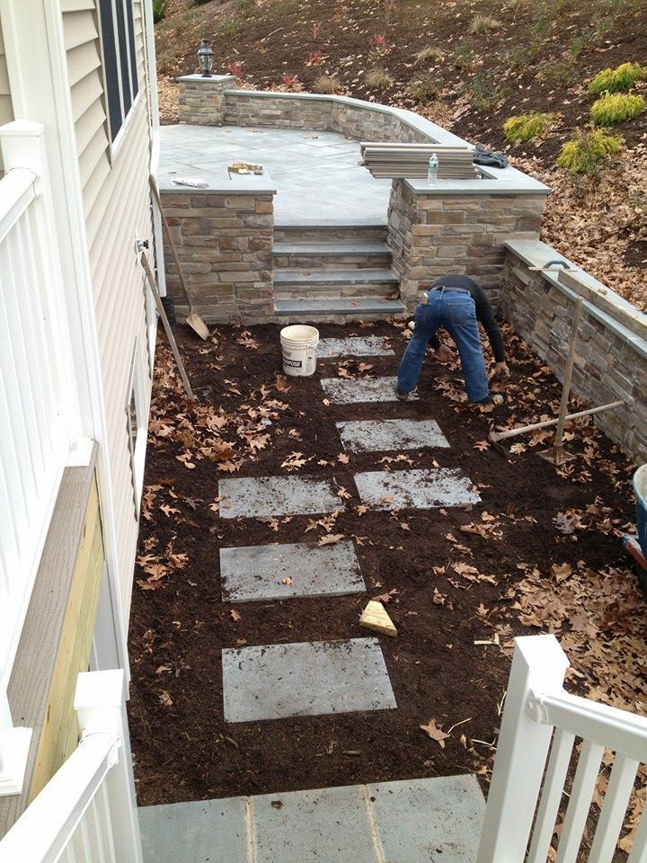 Person installing stepping stones leading to a patio with stacked stone walls and stairs.