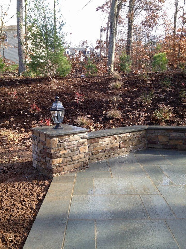 Stone patio with a low wall, lamp, and hillside garden.